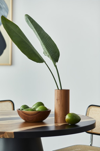 Minimalist composition on the design wooden table with fruits,
tropical leaf in vase, abstract painitngs and stylish chair