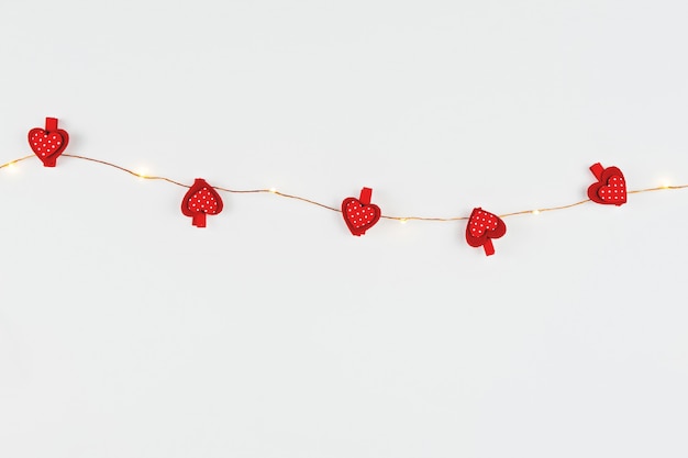 Minimalist composition with fairy light and red hearts on white