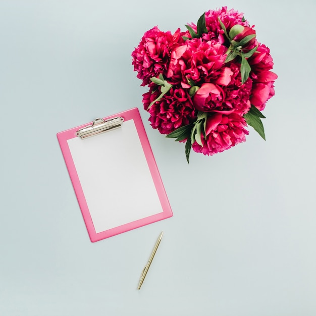 Foto scrivania da ufficio minimalista piatta con appunti, bouquet di fiori di peonia rosa su superficie blu