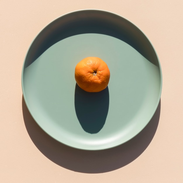 Minimalist image of a mandarin on a light green plate with a beige background