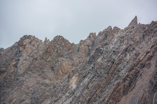 Фото Минималистский пейзаж с высокой скалистой горной стеной с остроконечными скалами в сером дождливом небе острые скалы и остроконечные вершины в сером облачном небе простой минимализм с горным хребтом с заостренными вершинами