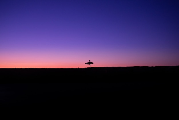 Fotografie minimaliste della silhouette di un surfista latino al tramonto su una spiaggia delle hawaii