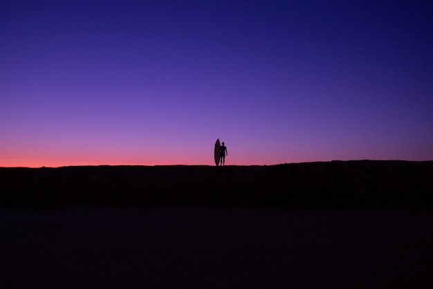 Foto fotografie minimaliste della silhouette di un surfista latino al tramonto su una spiaggia delle hawaii