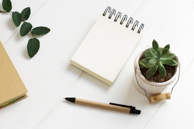 Foto area di lavoro minimalista con blocco note e penna e vaso per piante d'appartamento