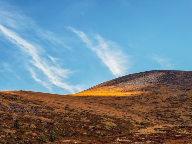 Minimalistic beautiful mountain scenery with golden light on slopes mountains. Scenic mountain landscape with illuminating color in blue sky.