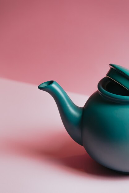 A minimalistic close up of a blue teapot over a pastel pink background