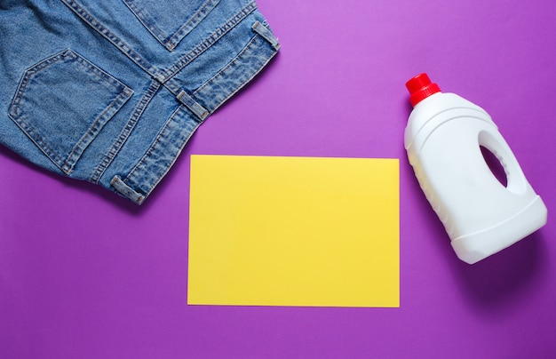 Minimalistic concept of washing. Paper for copy space, Jeans, bottle of washing gel on purple table. Top view