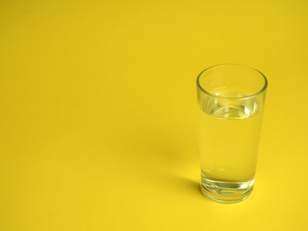 Minimalistic concept of water consumption, one glass of water on a yellow.