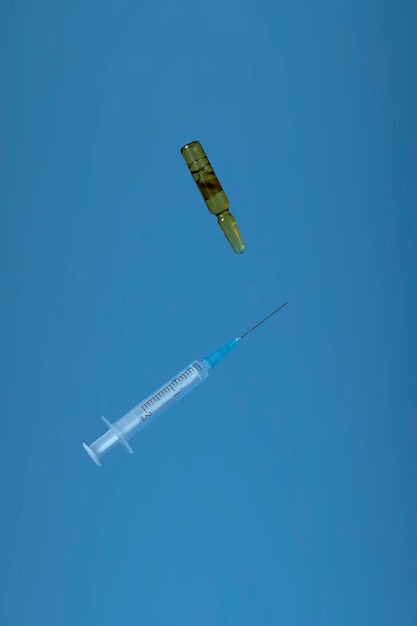 Minimalistic creative image with copy space. Medical concept vial with covid19 vaccine or medicine and syringe levitating on blue background. A bottle of vitamins recovery after covid19.