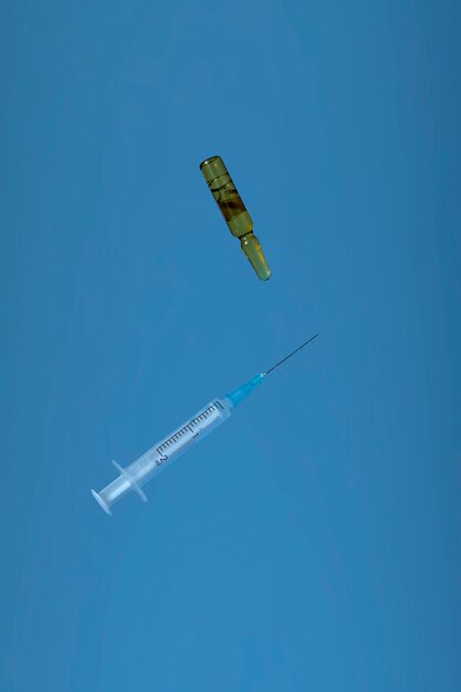 Minimalistic creative image with copy space. Medical concept vial with covid19 vaccine or medicine and syringe levitating on blue background. A bottle of vitamins recovery after covid19.