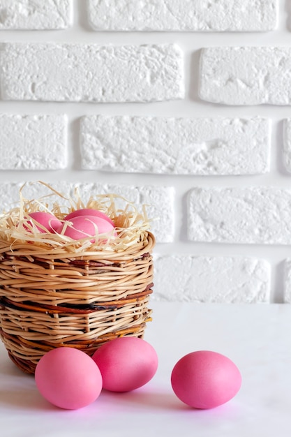 Минималистичная пасхальная композиция с плетеной корзиной и розовыми яйцами на белом фоне. Копировать пространство