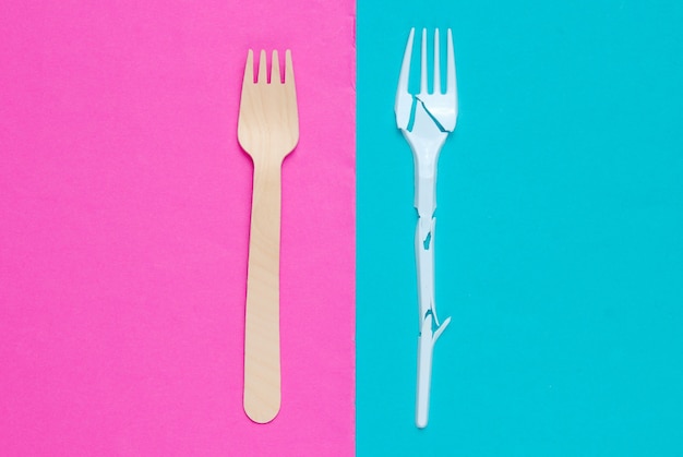 Natura morta ecologicamente pulita minimalista. forchetta di plastica rotta e forchetta di legno su sfondo rosa blu. posate realizzate con materiali naturali