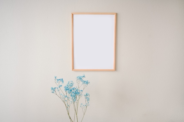 Minimalistic female still life art scene pastel colors. Empty picture poster mock up frame on beige wall, stylish composition with blue dry flowers