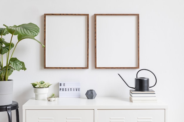 Minimalistic home decor of interior with two brown wooden mock up photo frames on the white shelf with books, beautiful plant in stylish pot and home accessories. White wall.