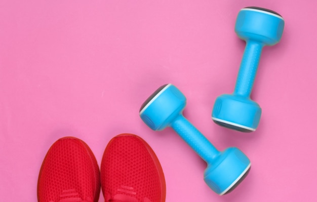 Minimalistic sport still life. sports outfit. red sports shoes\
for training and blue plastic dumbbell. top view