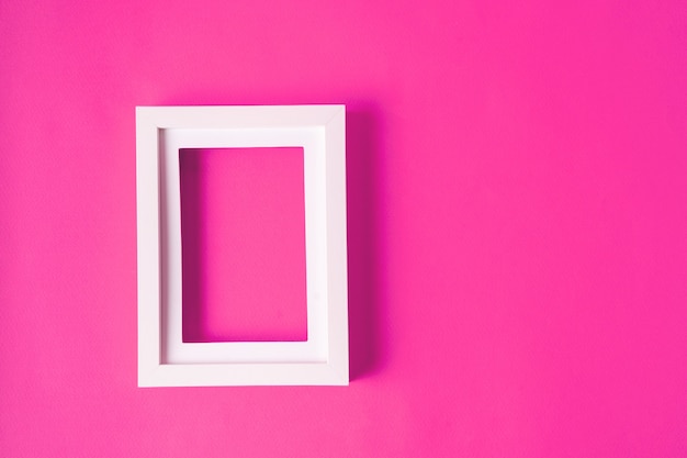 Minimalistic style. A white blank picture frame on pink background , flat lay.