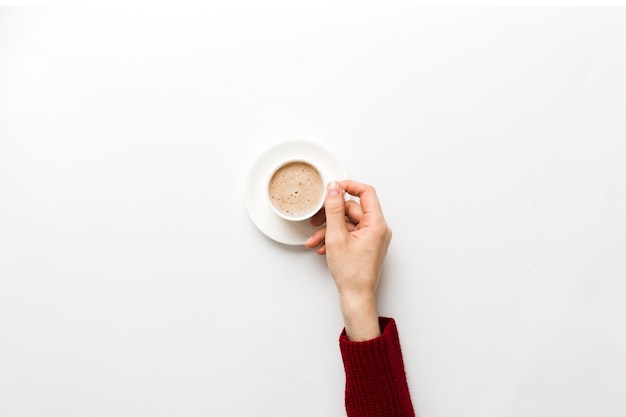 Minimalistic style woman hand holding a cup of coffee on Colored background Flat lay top view cappuccino cup Empty place for text copy space Coffee addiction Top view flat lay