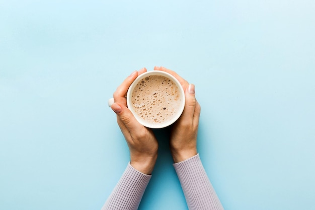 Minimalistic style woman hand holding a cup of coffee on Colored background Flat lay top view cappuccino cup Empty place for text copy space Coffee addiction Top view flat lay