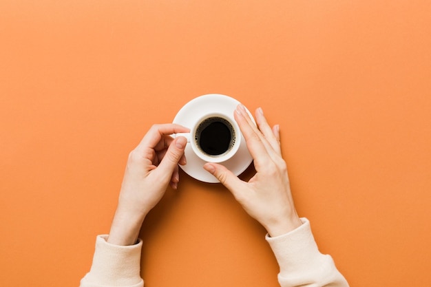 Minimalistic style woman hand holding a cup of coffee on Colored background Flat lay top view cappuccino cup Empty place for text copy space Coffee addiction Top view flat lay