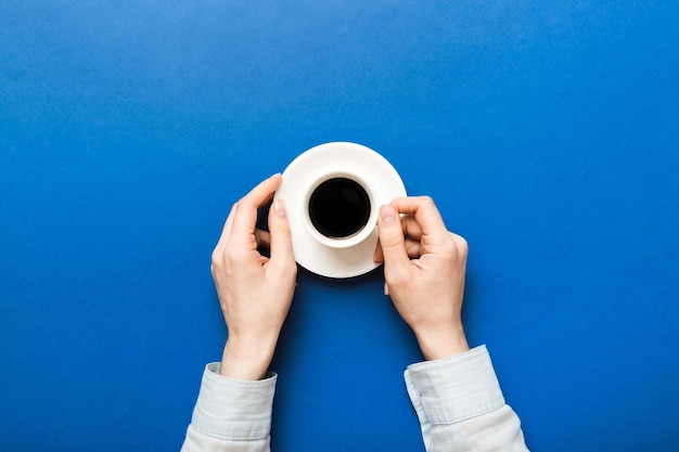 Minimalistic style woman hand holding a cup of coffee on Colored background Flat lay top view cappuccino cup Empty place for text copy space Coffee addiction Top view flat lay