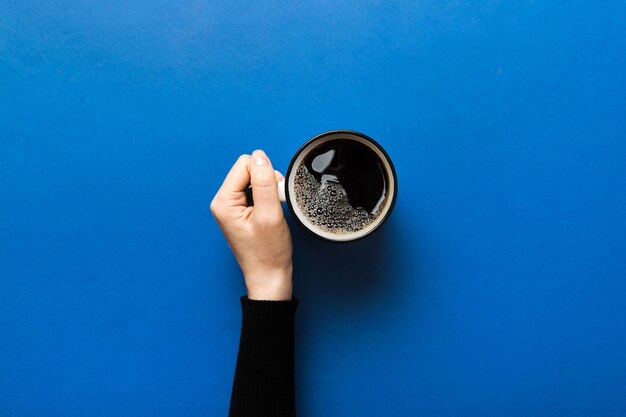 Minimalistic style woman hand holding a cup of coffee on colored background flat lay top view cappuccino cup empty place for text copy space coffee addiction top view flat lay