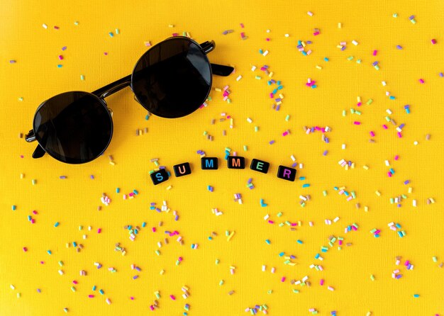 Minimalistic summer concept sunglasses and black beads on yellow background making word