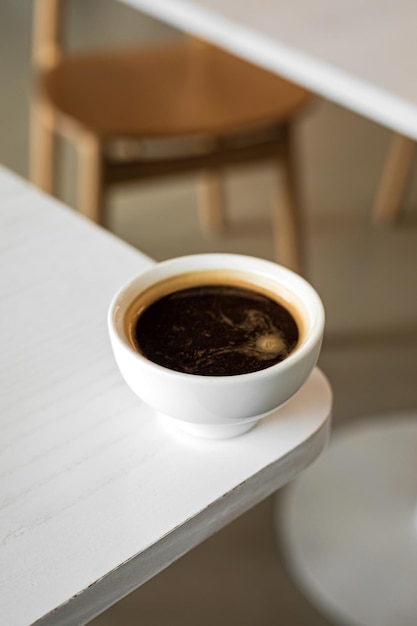 A minimalistic vertical image of a white cup of black coffee americano on the edge of a table in a cafe copy space