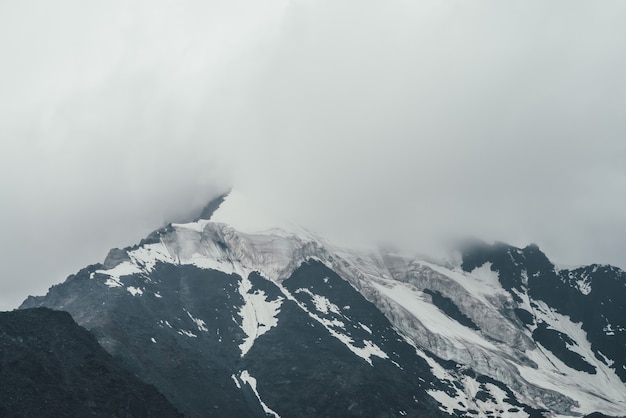 Minimalistisch monochroom atmosferisch berglandschap met grote besneeuwde bergtop in lage wolken. Geweldig minimaal landschap met gletsjer op rotsen. Zwart witte hoge bergtop met sneeuw in de wolken.