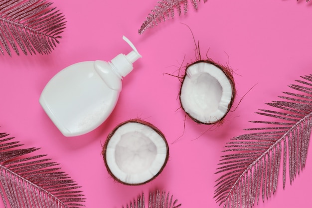 Minimalistisch schoonheidsstilleven. Twee helften van gehakte kokos en witte fles room met gouden palmbladeren op roze