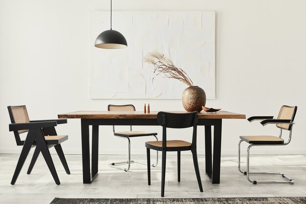 Foto minimalistische compositie van eetkamerinterieur met houten tafel, designstoelen, gedroogde bloemen in een vaas, zwarte hanglamp, kunstschilderijen aan de muur en elegante persoonlijke accessoires.