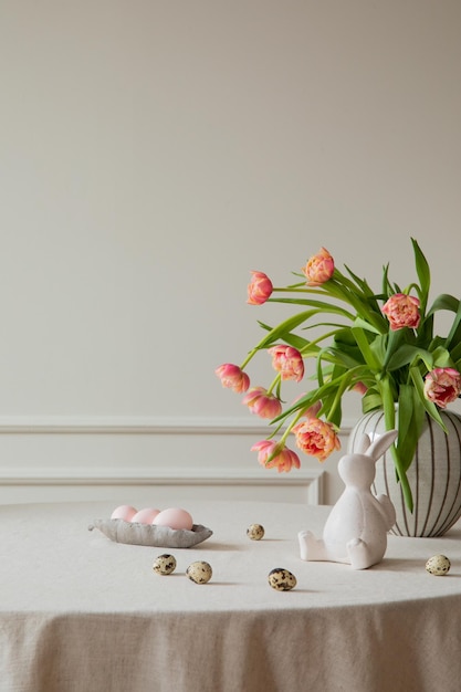 Minimalistische samenstelling van Pasen eetkamer interieur met kopie ruimte vaas met tulpen kleurrijke eieren grijze kip sculptuur beige muur met stucwerk en persoonlijke accessoires Home decor sjabloon