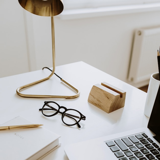 Minimalistische werkruimte met laptop, notebook, lamp, bril op witte tafel