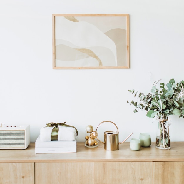 Minimalistische woonkamer in scandinavische stijl met fotolijst op witte muur houten tafel met geschenkdoos, eucalyptusboeket met kaarsen en radio