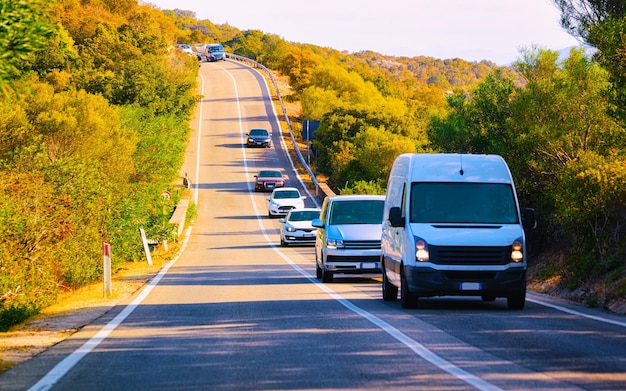 Minivan en auto's op de weg aan de Costa Smeralda aan de Middellandse Zee in de zomer van het eiland Sardinië, Italië. Minibusje op vakantie langs snelweg of snelweg. Gemengde media.