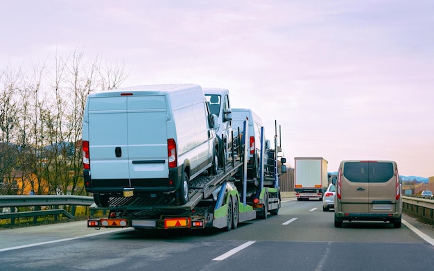 Minivan vervoerder vervoerder vrachtwagen op de weg. Auto voertuigen vervoerder op oprit. Europese bestelwagen transport logistiek bij goederenvervoer werk transport. Zware autoaanhangwagen met chauffeur op snelweg.