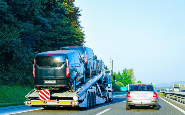 Minivans Car carrier transporter truck in road. Mini vans Auto vehicles hauler on driveway. European transport logistics at haulage work transportation. Heavy haul trailer with tow on highway.