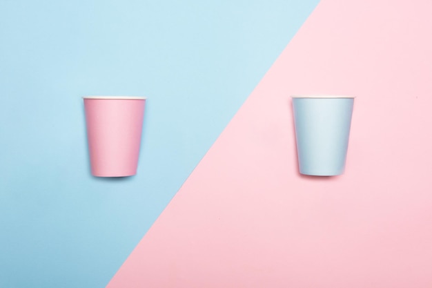 Mint blue and pink paper drinking cups on duotone pink and blue background. Minimalist pastel style