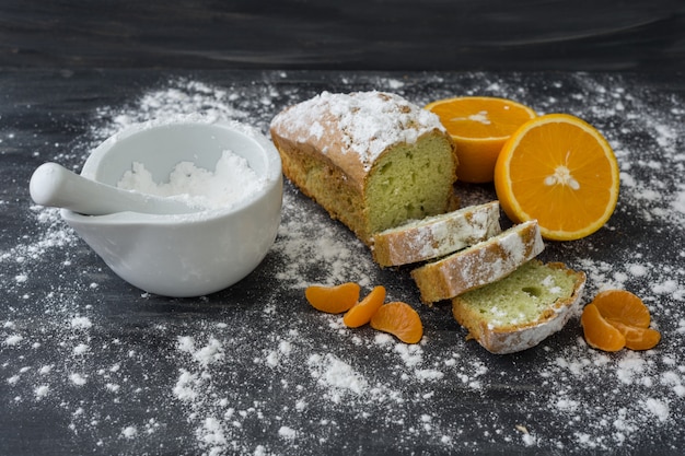 Mint cake sprinkled with powdered sugar on dark surface with fresh oranges mandarins