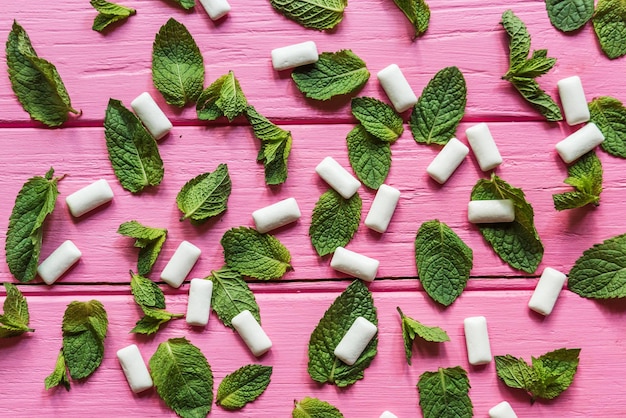 Mint gum and mint leaves on pink wooden background