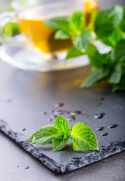 Foto foglia di menta. foglie di menta. tè. tè alla menta. tè alle erbe. tè in tazza di vetro, foglie di menta, tè essiccato, lime a fette. tisana alle erbe e foglie di menta su un piatto di ardesia in un ristorante o nella sala da tè della casa da tè