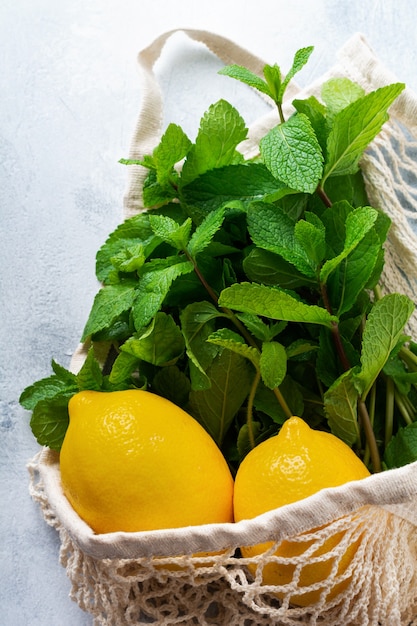 Mint leaves, fresh lemon and honey lying holding mesh shopping cotton bag on old gray concrete.