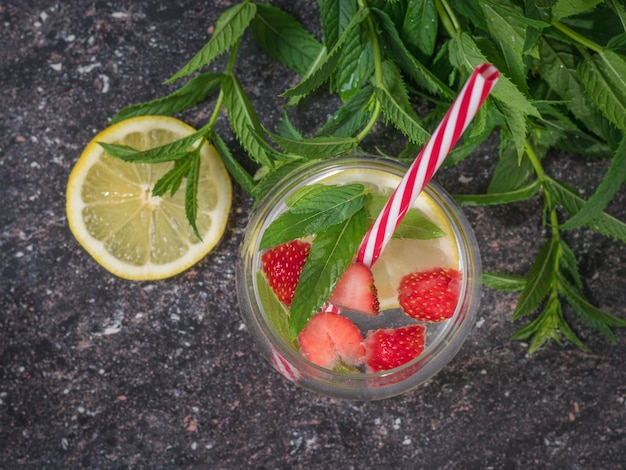 Foglie di menta e una tazza di acqua fredda con limone e frutti di bosco