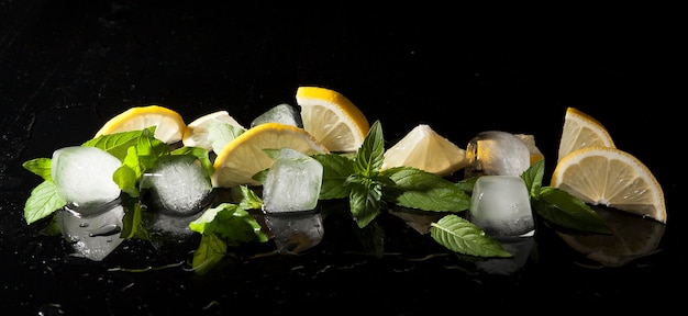 Мята, лимон и лед в брызгах воды на темном фоне