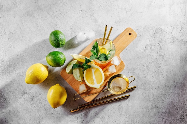 Mint, lime, lemons ice and bar utensils on wooden cutting board on white marble background top view