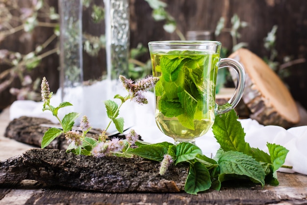 Tè alla menta in un bicchiere, erba su un tavolo di legno