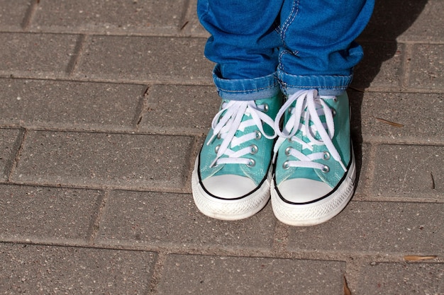 Mint youth sneakers, shod on legs in blue jeans, on paving city tiles