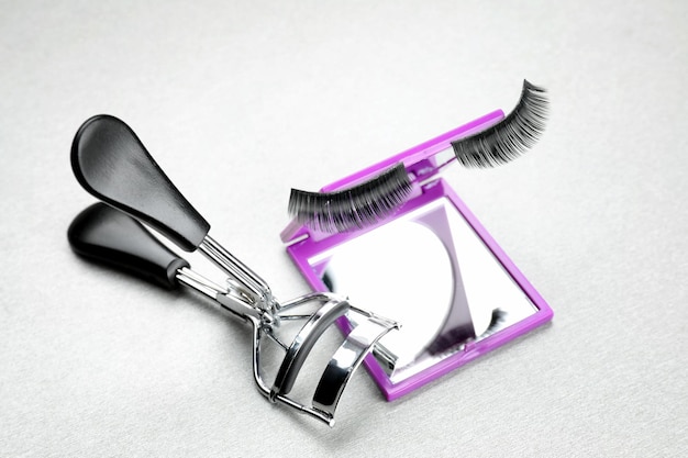Mirror with curler and false eyelashes on light background