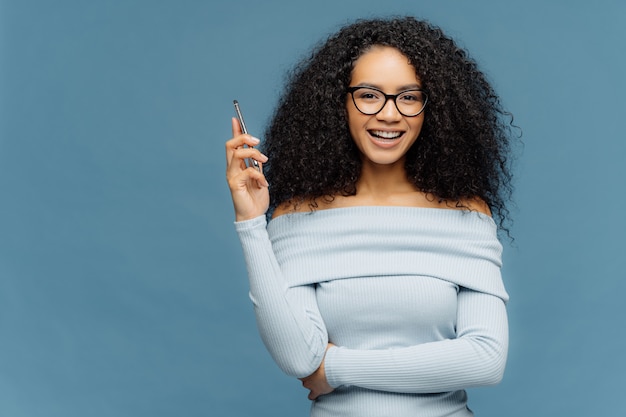 Mirthful Afro American woman holds smart phone, waits for call