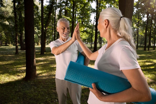 Mirthful aged man tenderly touching the hand of his wife while holding roll mat under his arm