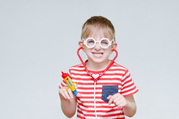 Mischievous boy playing doctor. Toy syringe, glasses and phonendoscope. Portrait